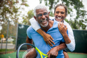 senior couple piggy back smiling on a tennis court